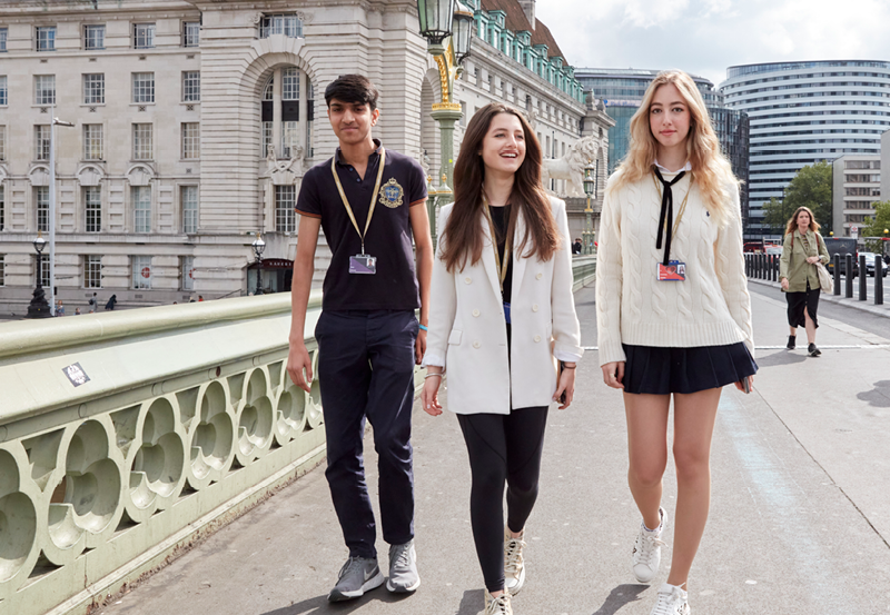 Студенты идут по Вестминстерскому мосту в Лондоне с колледжем DLD в Лондоне на заднем плане
